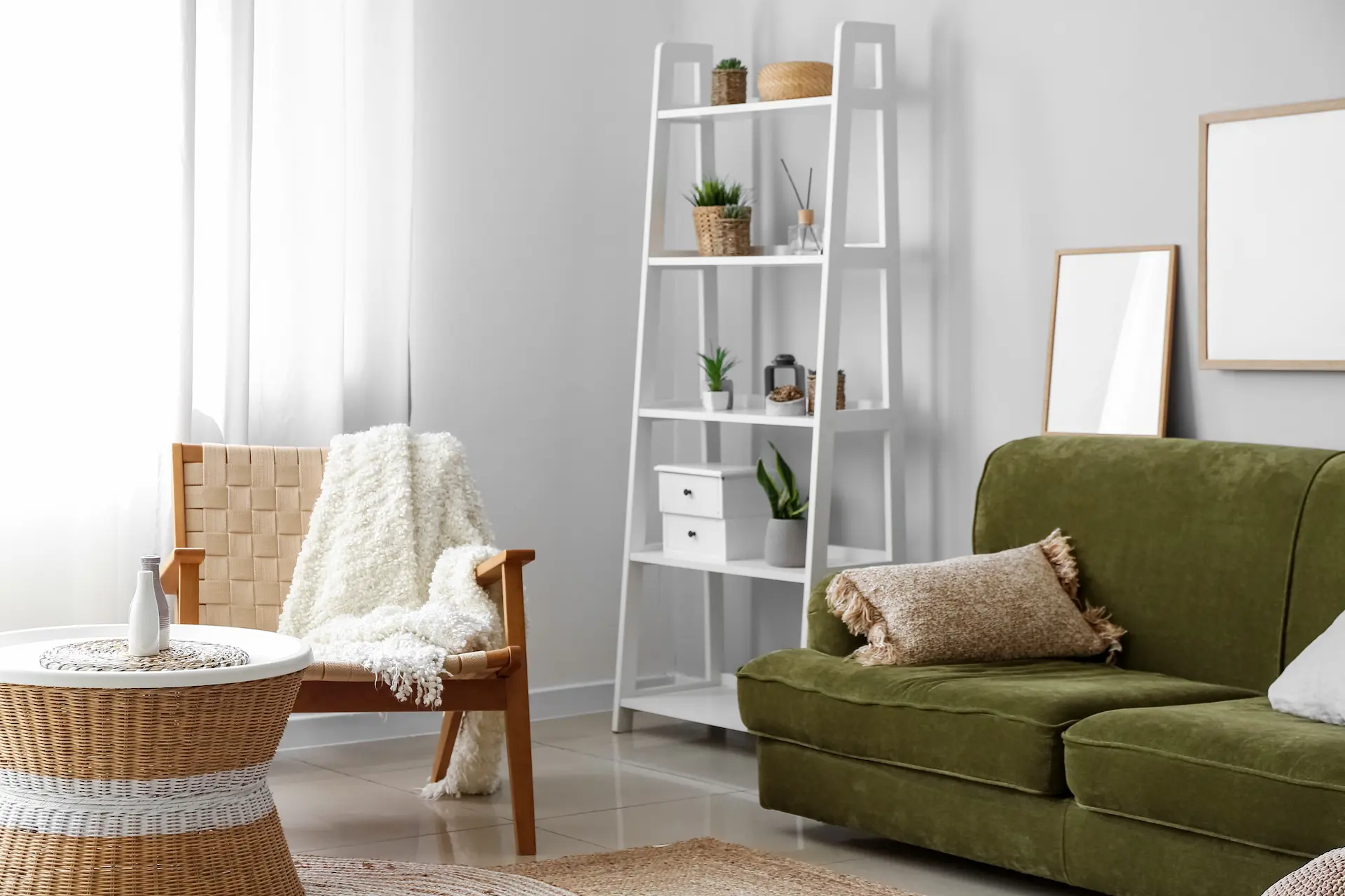 Salon chaleureux avec canapé vert olive, fauteuil en osier recouvert d'un plaid blanc et étagère en bois accueillant plantes et objets de décoration. Lumière naturelle douce.