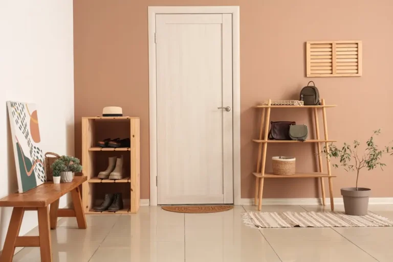 Entrée minimaliste avec porte en bois clair, murs beiges et sol carrelé. Des étagères en bois accueillent chaussures, sacs et objets de décoration. Une plante en pot apporte une touche de verdure.
