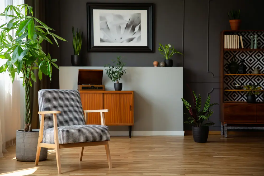 Salon chaleureux avec parquet, fauteuil gris, plantes en pot, meuble vintage, tableaux abstraits encadrés et bibliothèque. Ambiance calme et moderne.