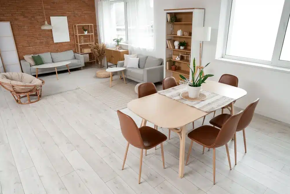 Espace de vie et salle à manger moderne et ouvert, avec parquet clair. Canapés confortables, plantes en pot et chaises marron créent une ambiance chaleureuse et accueillante.