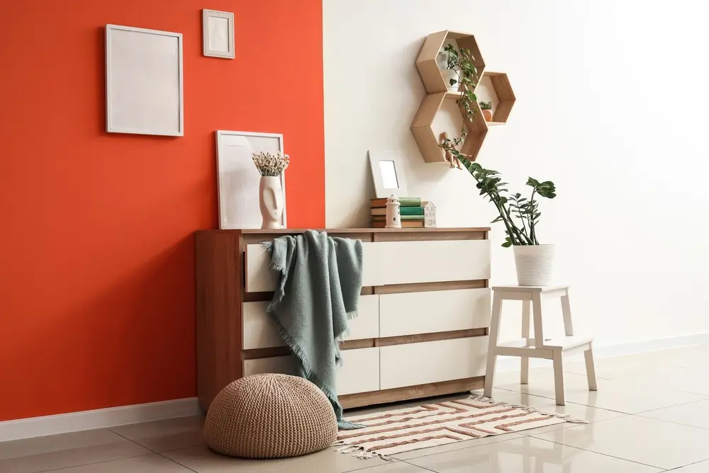 Salon moderne avec un mur rouge et blanc, une commode en bois ornée de décorations, des étagères hexagonales et des plantes. Les tons neutres créent une ambiance chaleureuse.