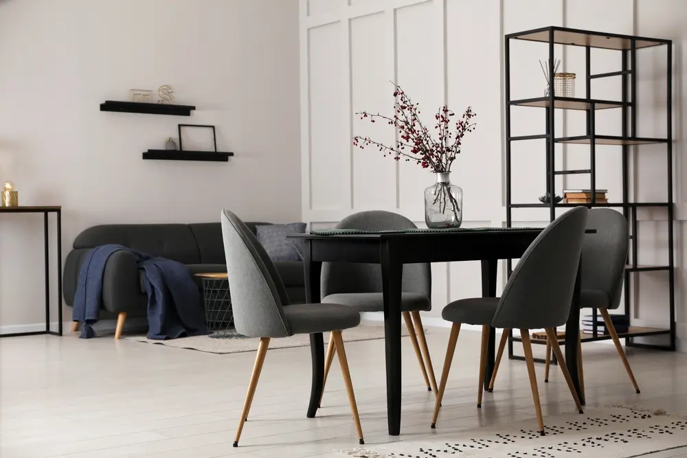 Salle à manger moderne avec une table noire et quatre chaises grises, agrémentée d'un vase de baies rouges. Décoration minimaliste comprenant des étagères et un canapé.